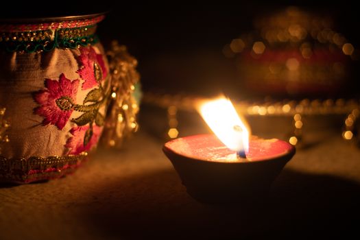 locked on shot showing a diya oil lamp burning bright on the hindu indian festival of diwali with beautiful bokeh in the background and decorative items nearby. Shows light chasing darkness on the symbolic victory of good over evil on the festival of deepavali and dussera in India