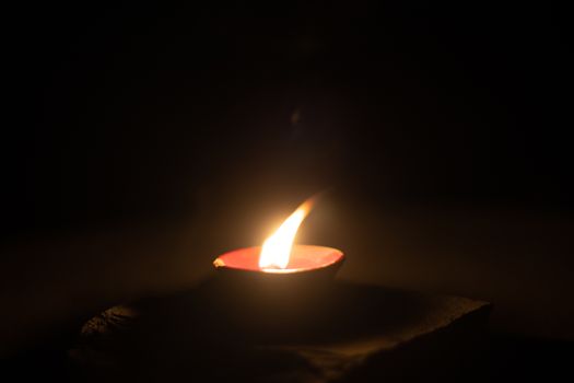 dark minimalistic image showing a diya oil lamp filled with oil or ghee and burning a cotton wick to produce a flame, its a popular religious item and decoration item on the hindu festival of diwali. This striking video shows it chasing away darkness in near total dark with plenty of copy space