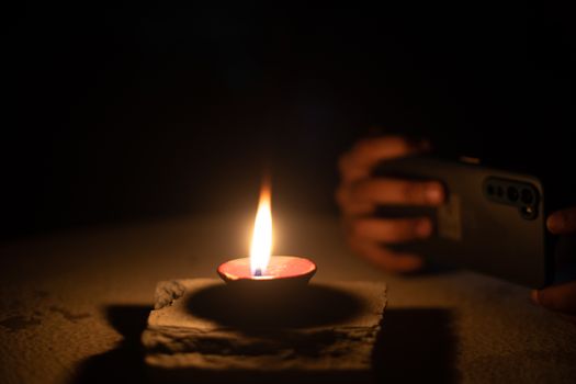 Man woman taking low light pictures of a diya oil lamp with a mobile phone for sharing images on the hindu festival of diwali. Shows the immense influence of social media and technology like low light capable cameras on traditional festivals like the hindu festival