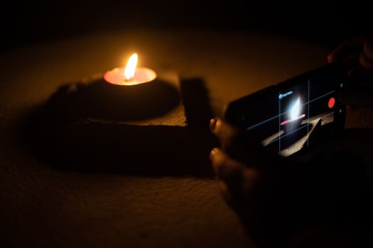 Man woman taking low light pictures of a diya oil lamp with a mobile phone for sharing images on the hindu festival of diwali. Shows the immense influence of social media and technology like low light capable cameras on traditional festivals like the hindu festival