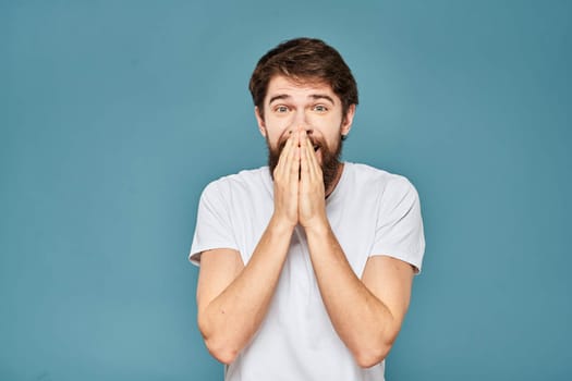 A bearded man in a white T-shirt gestures with his hands emotions blue background. High quality photo