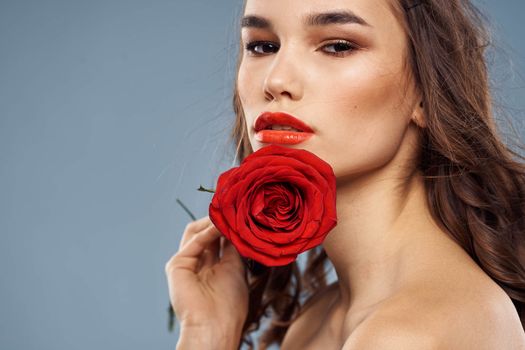 Portrait of a woman with a red rose in her hands on a gray background naked shoulders evening makeup. High quality photo