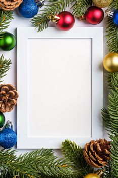 Christmas composition with empty picture frame. Colorful ball ornament, pine cones and fir needles decorations. Mock up greetings card template