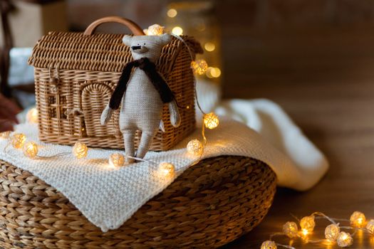 Teddy bear toy on the background of a wicker house made of rattan among Christmas garlands