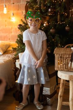 .Funny little girl in mask-glasses with a fir-tree on a christmas background in a loft interior