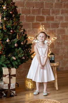 The adorable little girl in gorgeous dress standing near Christmas tree.