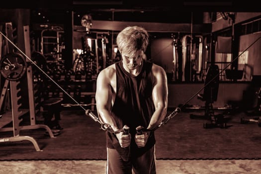 Strong fitness man doing arm workout with cable machine in the gym