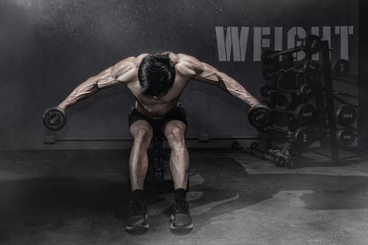 Strong fitness man doing arm workout with dumbbells in the gym