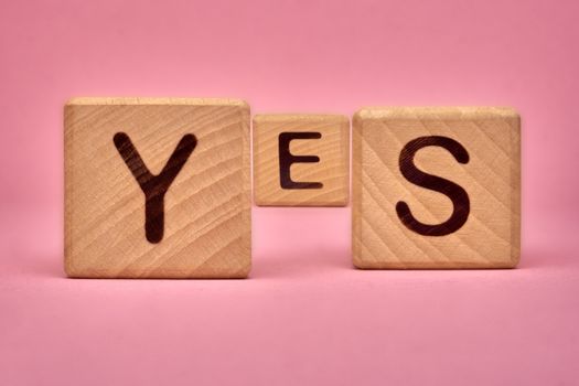 Wooden cubes with the word yes. Three wooden blocks with letters YES on pink background. YES text on pink background. Message of acceptance with yes word on monochrome background