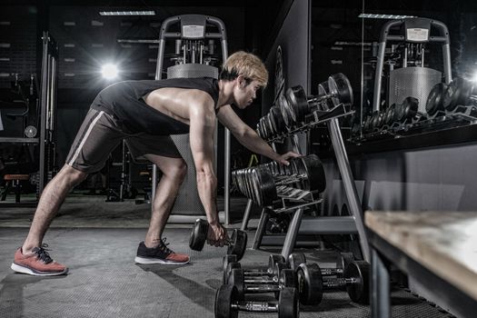 Strong fitness man doing arm workout with dumbbell in the gym