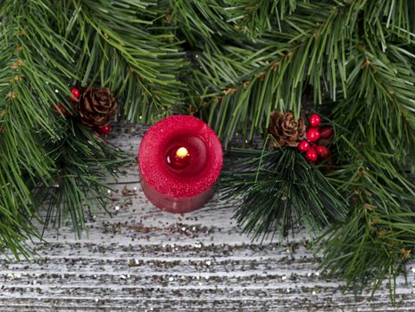 Closeup top view of a burning candle with pine cones and red berries surrounded in evergreen branches for the Christmas season 