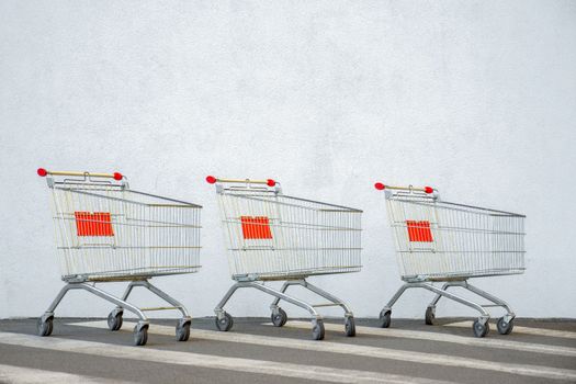 Three Empty Trolley at the Supermarket. Grocery Cart on the White Wall Store. Shopping Cart Trolley Stands near Mall with Copy Space. Black Friday Sale. Side View. Shopping Online. Shopping Concept