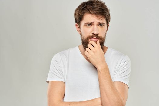 A man in a white t-shirt with a beard emotions displeased facial expression light background. High quality photo