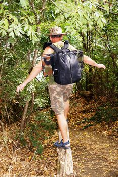 a man with a backpack crosses a ravine through a fallen tree.