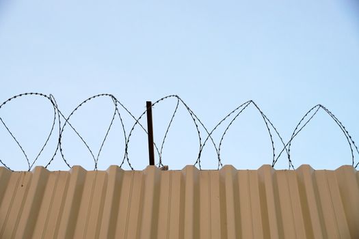fence with barbed wire in jail against blue sky.