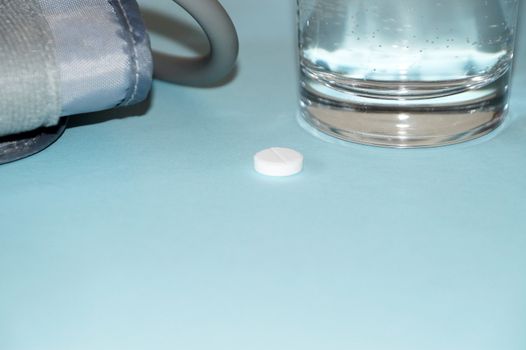 blood pressure monitor, glass of water and pill on blue background.