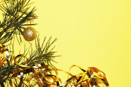 spruce branch with golden balls and tinsel on a yellow background, christmas card, copy space