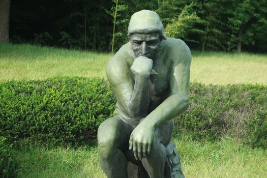 CHUNCHEON, SOUTH KOREA- JANUARY-10, 2019: Green statue of thinker Auguste Rodin, setting naked on a rock in a public park