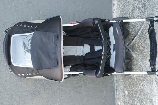 Black color baby stroller with head covering. Stroller is with concrete background