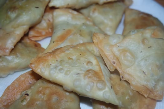 Closeup of delicious home made spicy and crunchy samosa pastries placed in a white ceramic plate on wooden floor