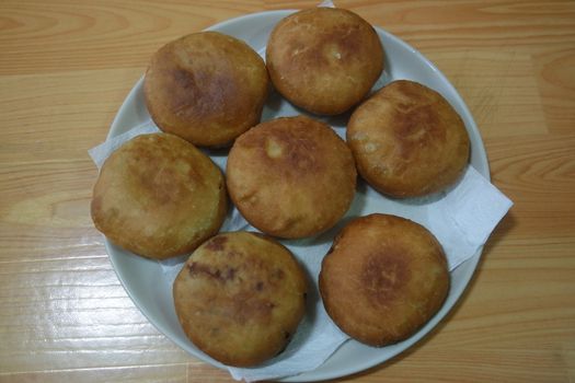 Closeup view of homemade tasty potato bread rolls bun placed in a white plate over a wooden floor.