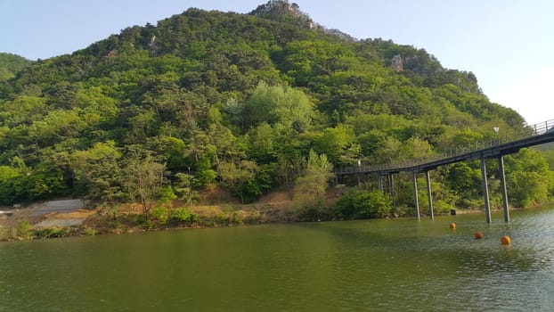 View of beautiful scene of river water and green trees on large hills on a sunny day with blue sky in background. A lovely landscape with breathtaking view over the horizon .