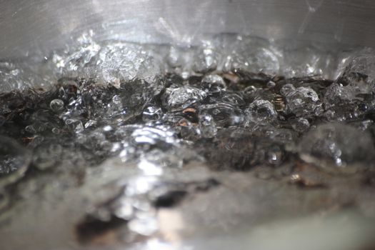 Closeup macro photograph with selective focus of boiling water in a metal pan