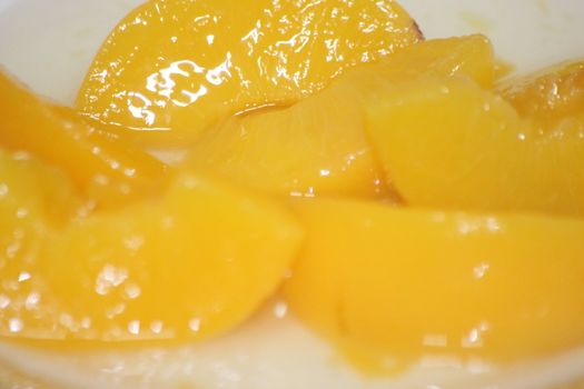 Closeup high angle view with selective focus of yellow peaches slices. Canned peaches halves sprinkled with syrup in white plate.