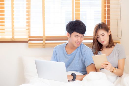 Beautiful young asian couple cheerful freelance working with man using laptop and woman using tablet on couch, family relax and sharing communication together at home, lifestyle concept.