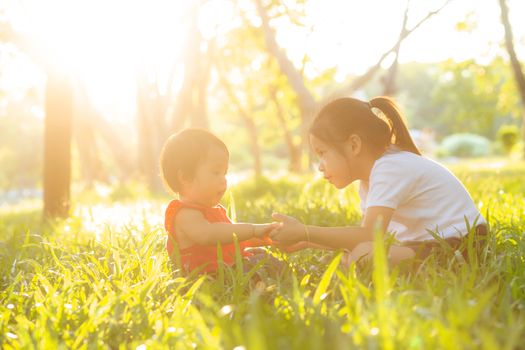 Beautiful young asian kid sitting playing in summer in the park with enjoy and cheerful on green grass, children activity with relax and happiness together on meadow, family and holiday concept.