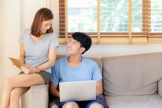 Beautiful young asian couple cheerful freelance working with man using laptop and woman using tablet on couch, family relax and sharing communication together at home, lifestyle concept.