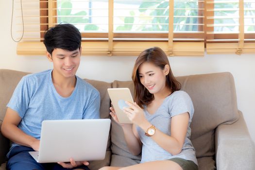 Beautiful young asian couple cheerful freelance working with man using laptop and woman using tablet on couch, family relax and sharing communication together at home, lifestyle concept.