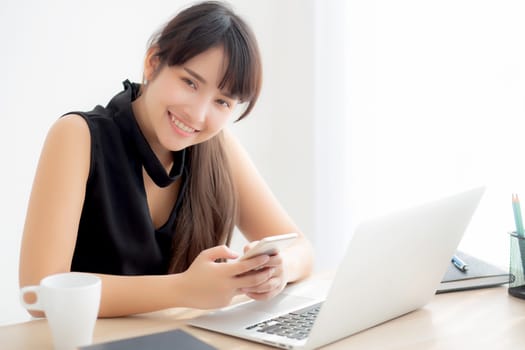 Beautiful young asian woman working laptop computer online to internet and texting message on smart mobile phone, freelance using notebook, business and communication concept.