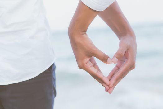 Closeup hand heart shape of young couple gay holding together on the beach in summer in vacation, happy asia Homosexual having love, LGBT of relationship legal and valentine day concept.
