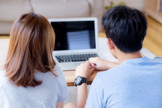 Back view of young asian couple working laptop with blank screen display, family planning and searching content together, man and woman looking computer, business and communication concept.