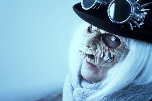 Woman with monster face and black hat wearing steampunk glasses. White hair.