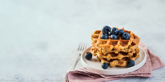 Easy healthy gluten free oat waffles with copy space. Stack of appetizing homemade waffles with oat flour decorated blueberries, on plate over light gray cement background. Banner