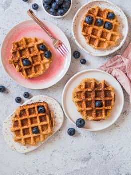 Easy healthy gluten free oat waffles with copy space. Plates with appetizing homemade waffles with oat flour decorated blueberries, on light gray cement background. Vertical. Top down view or flat lay