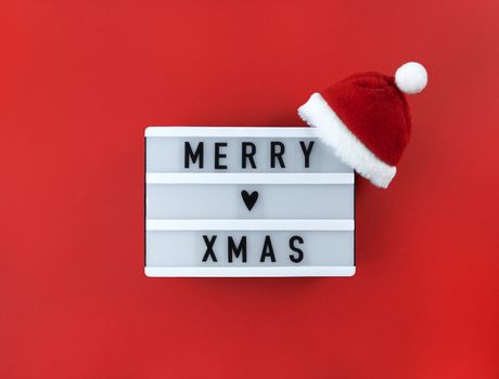 Merry xmas greeting on a light box with Santa hat on a red background.