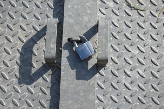 Checkered diamond patterned galvanized steel plates, lit by natural sunlight in an outdoor setting. Shiny metal padlock sits between the two handles