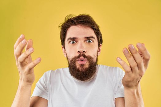 A man in a white t-shirt gestures with his hands lifestyle cropped view yellow background more fun. High quality photo