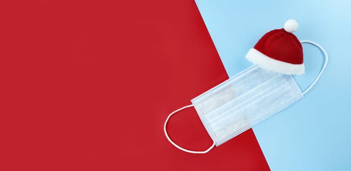 Medical mask and Santa Claus hat on red, blue background.