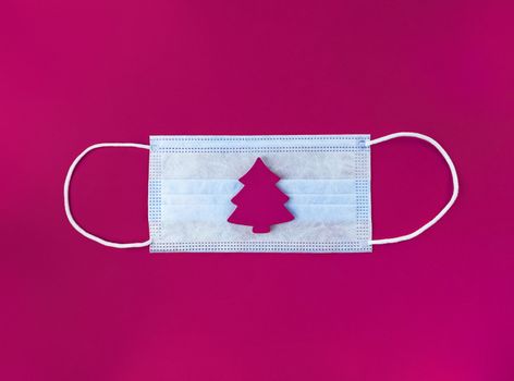 Medical mask and wooden christmas tree on magenta background.