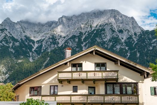 Mittenwald, Bavaria/Germany - 15.08.2020: A big beautiful house with balcony and many windows in front of a huge mountain range, which is lost in clouds.