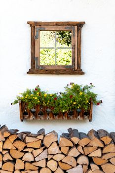 A decorative window on a house wall over a flower box and firewood, which gives a nice picture from the street