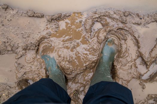 feet in green rubber boots stands in wet brown mud directly above view, directly above first person gonzo view
