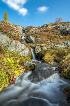 Beautiful low angle shot of waterfall in Altai mountains in Siberia, Russia. Karakolskie lakes. Smooth, silky water and clouds. Blue sky with clouds as a background on top of the hill. Long exposure.