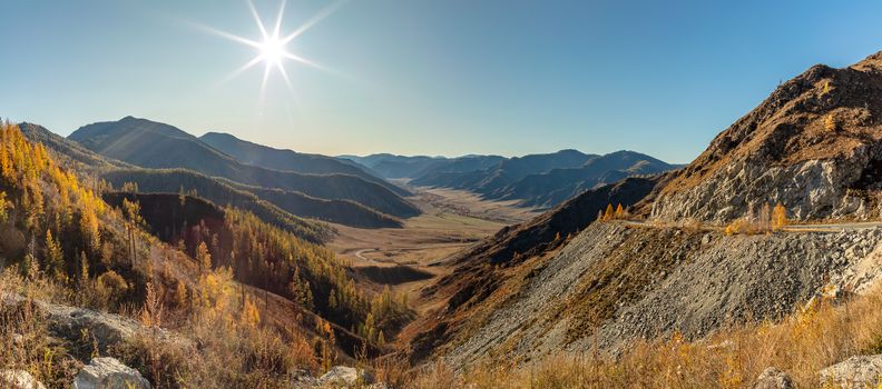 Altai mountains. Beautiful highland autumn panoramic landscape. Rocky foreground with golden trees. Blue sky with the sun as a background. Russia. Siberia.