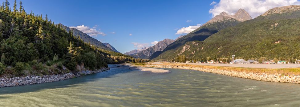 View of Skagway River and Skagway airport at sunset in Alaska. Golden hour. Blue cloudy sky and mountain peaks in the background.