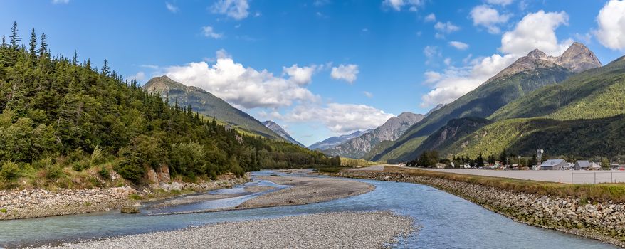 View of shallow Skagway River and Skagway airport in Alaska. Blue cloudy sky and mountain peaks in the background.